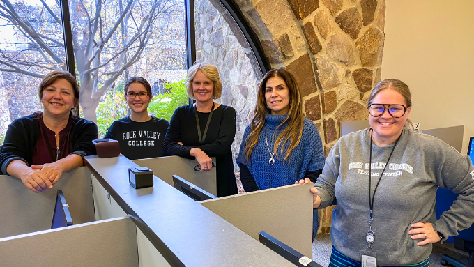 The testing center staff, consiting of five women, stand beside testing cubicles in the center.