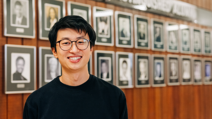 Bing Liu, RVC 2023 Distinguished Alumnus, standing in front of the RVC Distinguished Alumnus wall at Rock Valley College.